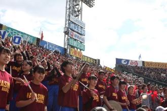 お揃いのえんじ色のTシャツをきて、立ち上がって応援をしている習志野高校の応援団の皆さんの写真