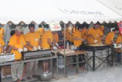 黄色のTシャツを着たボランティアの方がテントの中で焼き鳥や焼きそばを販売している写真