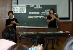 黒板の前に2人の女性が立ち手話をしている講座の写真