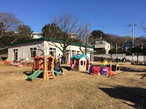 奥に白い外壁に緑の屋根、園庭の芝生の上にはたくさんのカラフルな遊具がある習志野市こどもセンターの園庭の写真