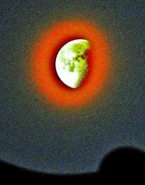 白色に緑色を帯びた月の周りを鮮やかな赤みがかった月周囲の花粉光環の写真