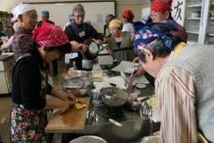 参加者がエプロンと三角巾を付けて調理台で包丁など使い作業している写真