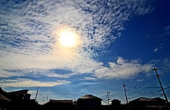 立ち並ぶ家の上に、うろこ雲から太陽の光が透けて見える空を写した写真