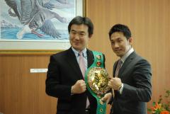 チャンピオンベルトを肩にかけガッツポーズの宮本市長と粟生選手が並んで写っている写真