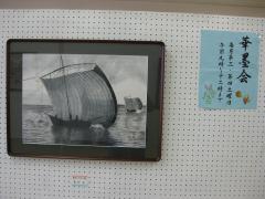 ボードに額に入った墨絵の帆曳船の絵が飾られている写真
