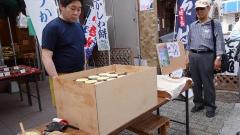 和菓子屋の店先にある木の箱に入った和菓子とその前に立つ男性の写真