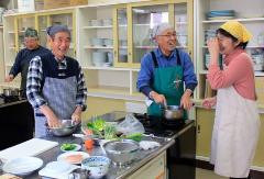 年配の男性メンバーと滝口先生が楽しく談笑しながら調理している様子の写真