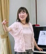 講師の真鍋久美好先生が左手をピアノに置き、右手でリズムを取っている様子の写真