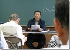 黒板の前に座って話しをしている桶田講師の写真