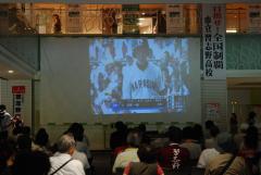甲子園の様子を大きなスクリーンの前で応援する方々の写真