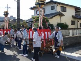 お揃いの法被を着た男性が紅白の幕がついた四神旗の山車を引いている写真