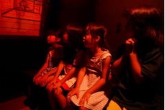 オレンジ色の照明のなか、4名の子どもたちが並んで椅子に座っている写真