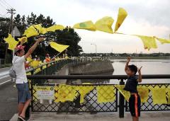 柵に設置されている黄色いハンカチの横で子どもが手を上にあげている写真
