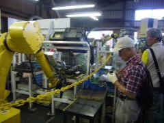 プレス機械を黄色の溶接ロボットが動かしている所を見学している参加者の写真