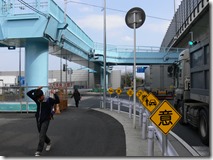 青い歩道橋の下には事故防止の黄色い看板が設置されている写真