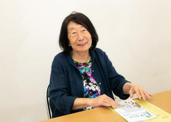 椅子に座り机に置かれたKIRACOに手を添えている井手郁子さんの写真