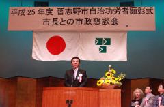 イベント名が書かれている横断幕の下に国旗と市旗が掲げられたステージの壇上でスピーチをする市長の写真