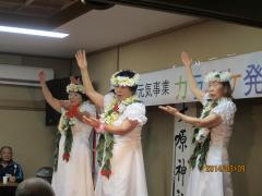 白い衣装を着て、頭と首に花飾りをつけフラダンスをうたう3人の女性の写真