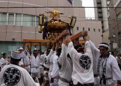 神輿を高く上にあげている白い法被を着た男性たちの写真