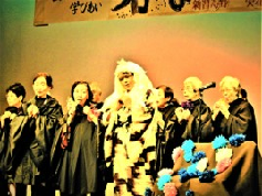 ステージ上で、黒いマントを被った人達と、歌舞伎の格好をした人が立っている大久保 花咲き山まつりの写真