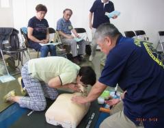 人口呼吸の訓練用のマネキンを使って実技訓練をしている参加者と横でレクチャーしている指導員の写真