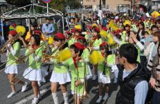 赤いベレー帽、黄緑色と白の衣装を着て楽器を演奏したり黄色いポンポンをもって歩いている実籾小学校吹奏楽部の写真
