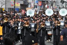 黒い衣装を着て町中を演奏しながら行進している第四中学校吹奏楽部の写真