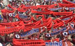 観客席で習志野と書いた赤いタオルを掲げて応援している人達の写真
