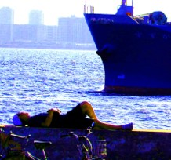 海には大きな船が進んでおり、岸壁に寝転んで日焼けを楽しむ人の写真