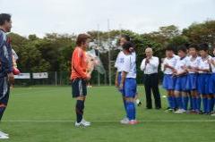 サッカー場で香澄小学校の女子児童がなでしこジャパンの代表選手に花束を手渡ししている写真