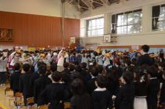 在校生が新一年生の前に並んで立ち、両手を上に挙げて踊りながら、在校生から新一年生へ歌のプレゼントをしている写真