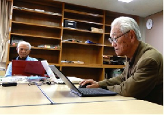 部屋の中でパソコンを操作している高木さんと赤澤さんを写した写真