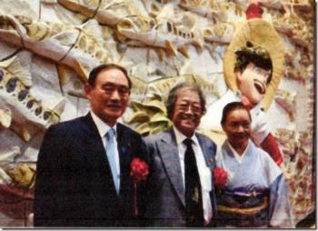 陶板レリーフ前で左から菅官房長官、矢口先生ご夫妻が並んで記念撮影をしている写真