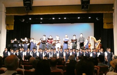 舞台上と舞台の下に日韓の高校生が並び、演奏と歌を披露している様子の写真