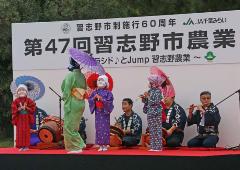 舞台上で太鼓や笛を演奏している菊田神社囃子連と和傘をさし着物を着て踊りを披露している女性と子供の写真