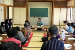 和室に2列に並べられた長机に参加者の人達が座り、前方の有馬和子さんの講演を聞いている写真