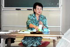 座布団に座りマイクを片手に話をしている講師の有馬和子さんの写真