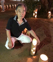 優しい光が灯された竹灯籠の横にしゃがんでいる代表の尾曽さんの写真