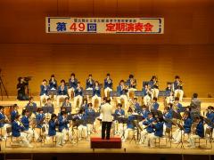 ステージ上で青色と白色の衣装を着た吹奏楽部員が演奏を行っている写真