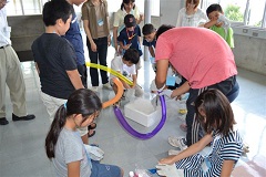 紫色、オレンジ、黄色の風船を使って参加者の子供達が実験を見ている写真