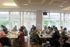 いくつかのテーブルに分かれ、学食をおいしそうに食事する参加者の人達の写真