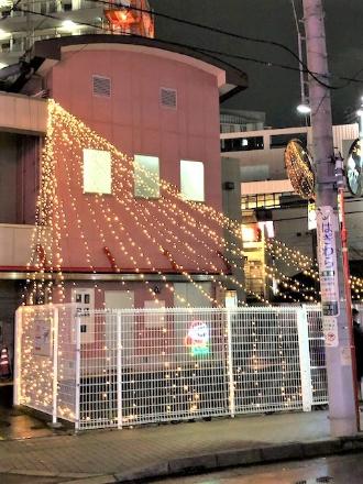 会館まえの2階からフェンスに向かってツリー状に電飾が伸ばされオレンジ色の光できれいに装飾されている津田沼一丁目町会会館前の写真