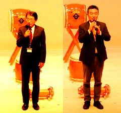 舞台上で、スーツ姿でマイクを持って挨拶をしている伊東館長（右）、宮本市長（左）の写真