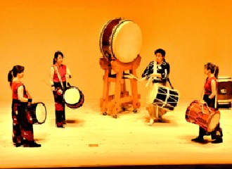 台座の上に乗せられた大きな平太鼓が中央に置かれ、太鼓を肩からさげた4人の演奏者が和太鼓の演奏を披露している写真