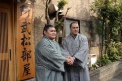 阿武松部屋の前で、2名の関取が両手を取り合って握手をしている写真