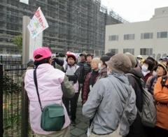 庄司ケ池史跡でピンク色のキャップにジャケットを着た女性スタッフの説明を熱心に聞いている参加者の写真