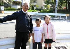 ガードレールを背に、佐久間校長先生と男の子と女の子の隊員が並んで立っている写真