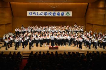 ホールの舞台上で生徒の皆さんが楽器を演奏している「ならしの学校音楽祭」の写真