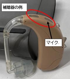 茶色の本体に透明のチューブとイヤーチップのついた耳掛け型の補聴器の本体上部にあるマイクを赤い枠で囲んでいる写真