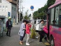 ランドセルを持つ人と後ろから誘導する人で子供がバスに乗るのを補助している写真